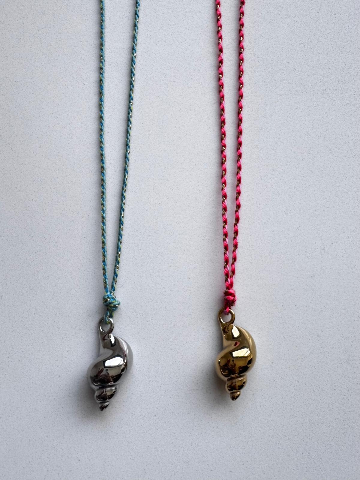 Colares com pendentes em forma de concha, um prateado e outro dourado, com cordões azul e vermelho.