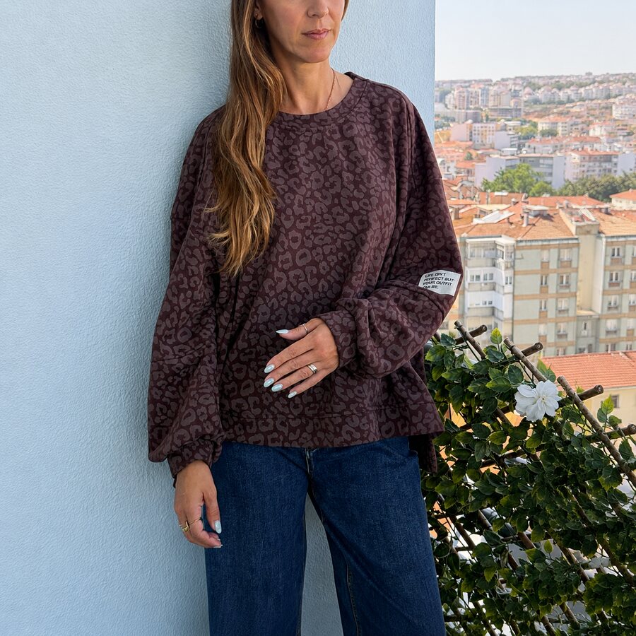 Sweatshirt castanha com padrão animal print e etiqueta, mulher no terraço urbano
