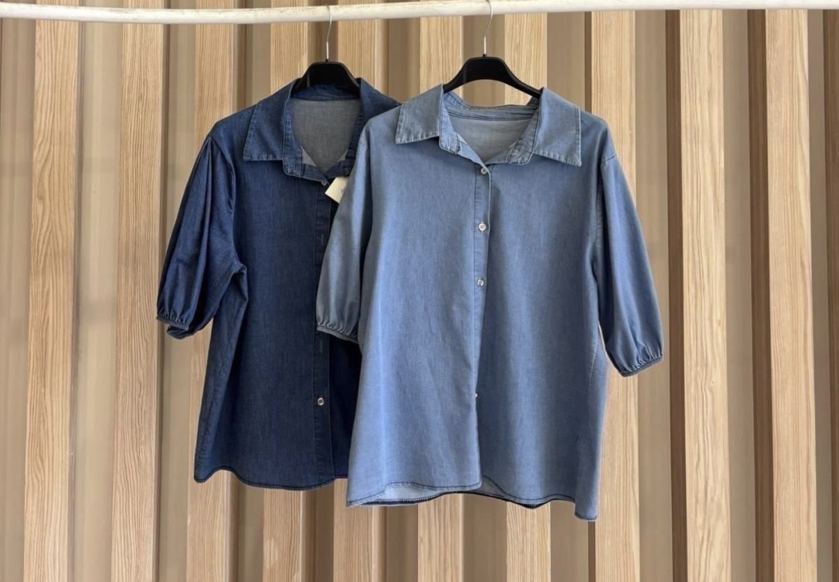 Duas camisas de ganga azul claro e escuro penduradas em cabides sobre painel de madeira