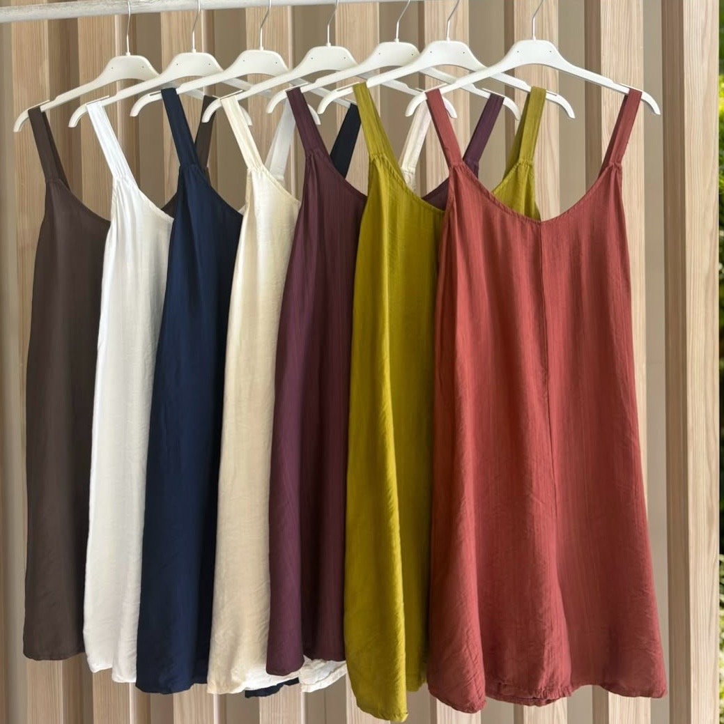 Vestidos de alças em várias cores pendurados em cabides brancos num varão de madeira