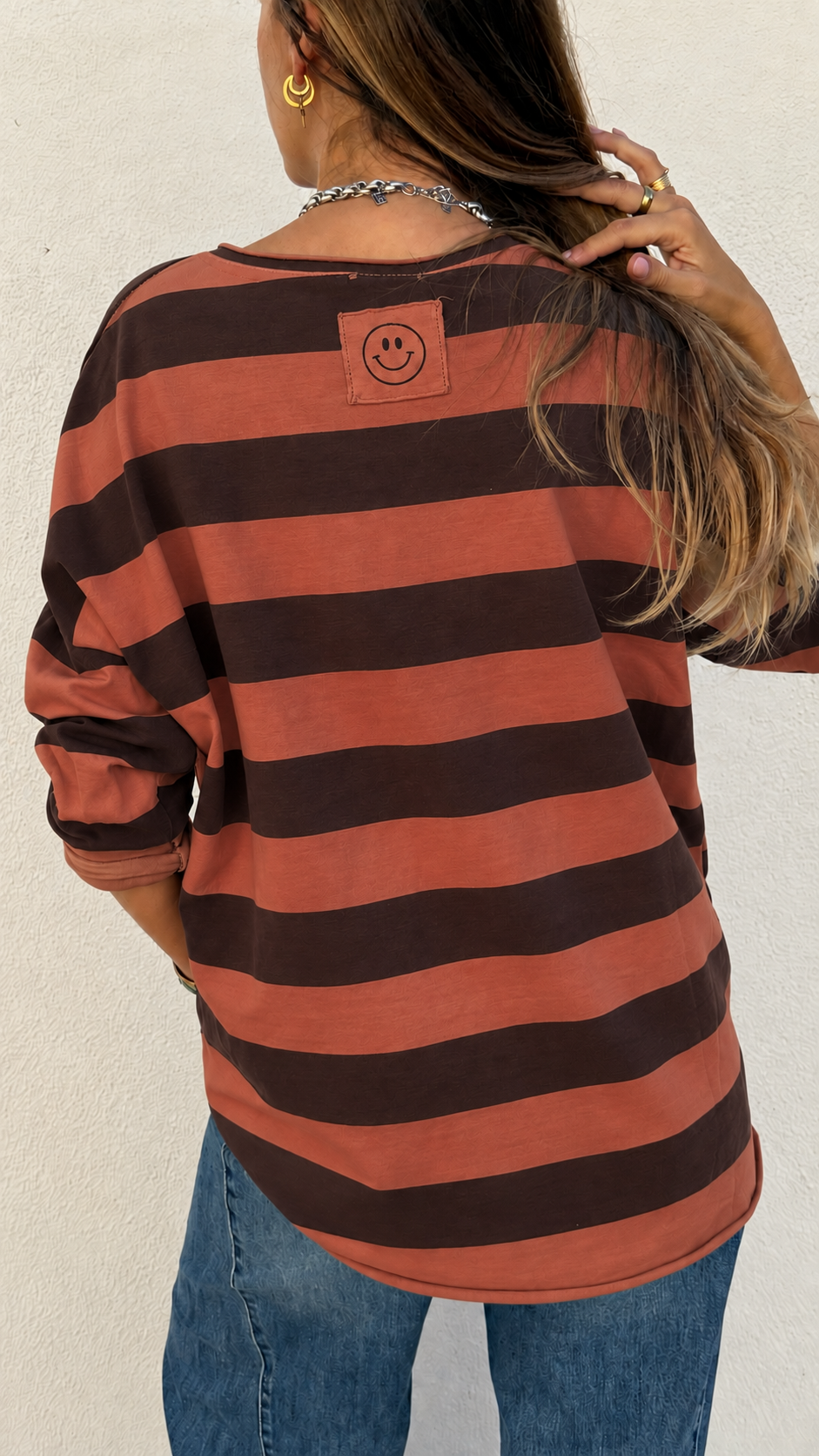 T-shirt riscada castanho e laranja com smiley nas costas e jeans azuis