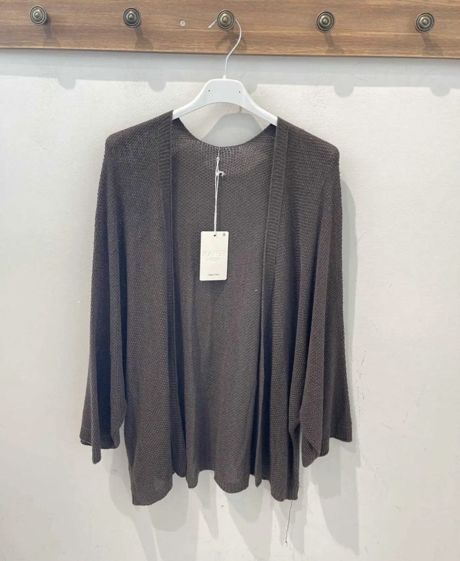 Cardigan castanho em malha fina pendurado num cabide branco numa parede com cabideiro de madeira