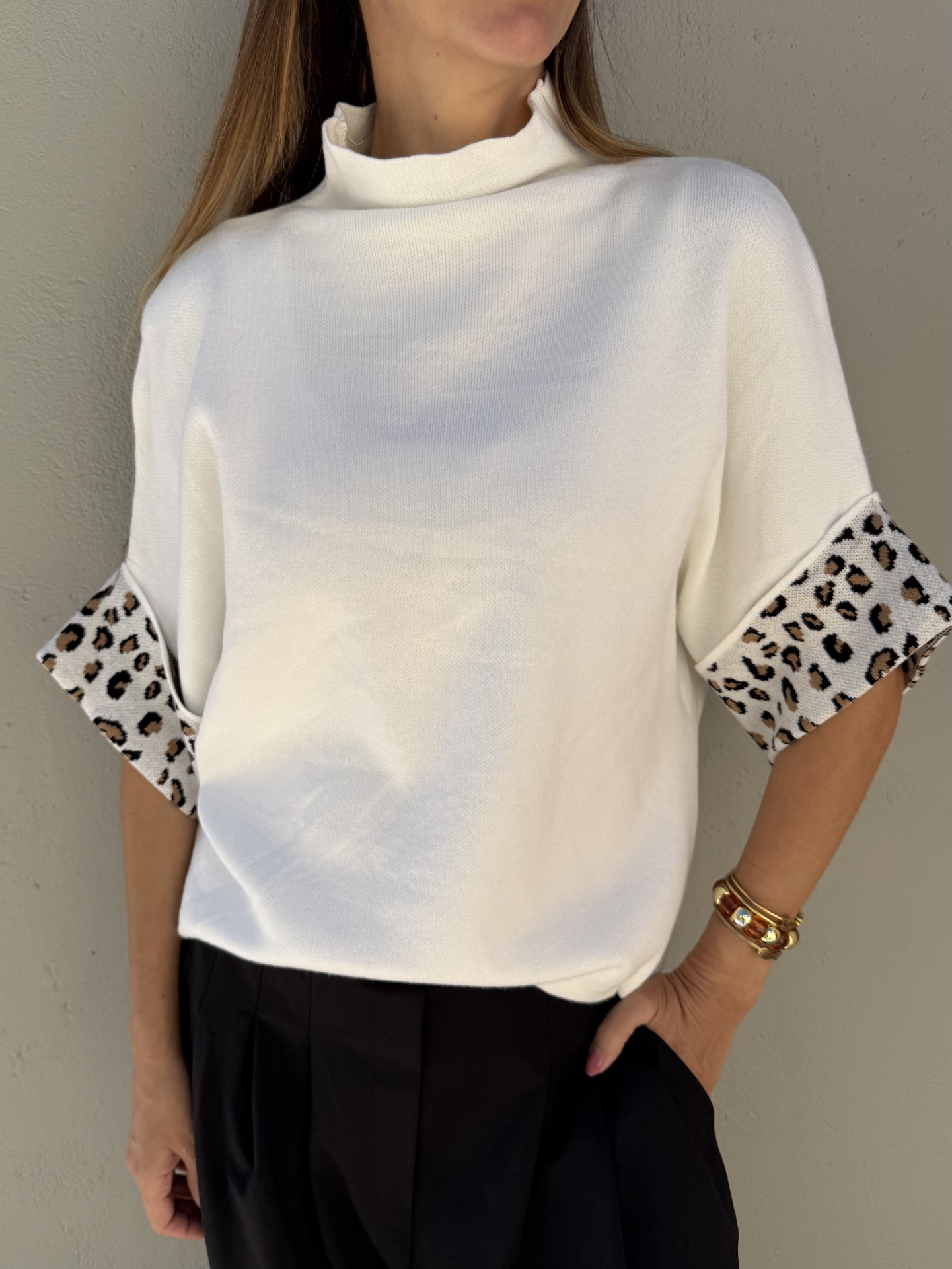 Camisola branca com punhos animal print e calças pretas num fundo cinza