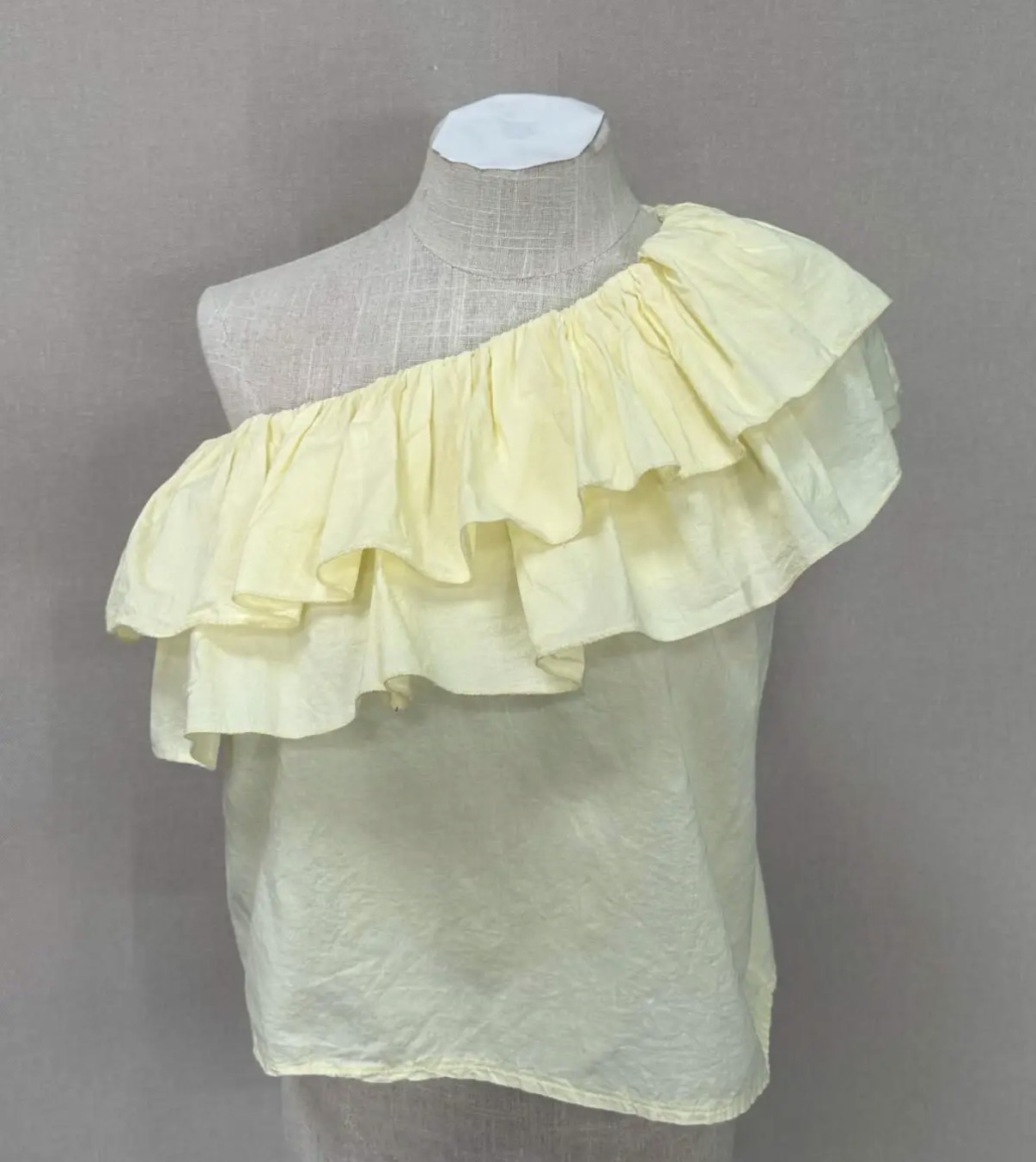 Blusa feminina amarela ombro único com babados numa manequim.
