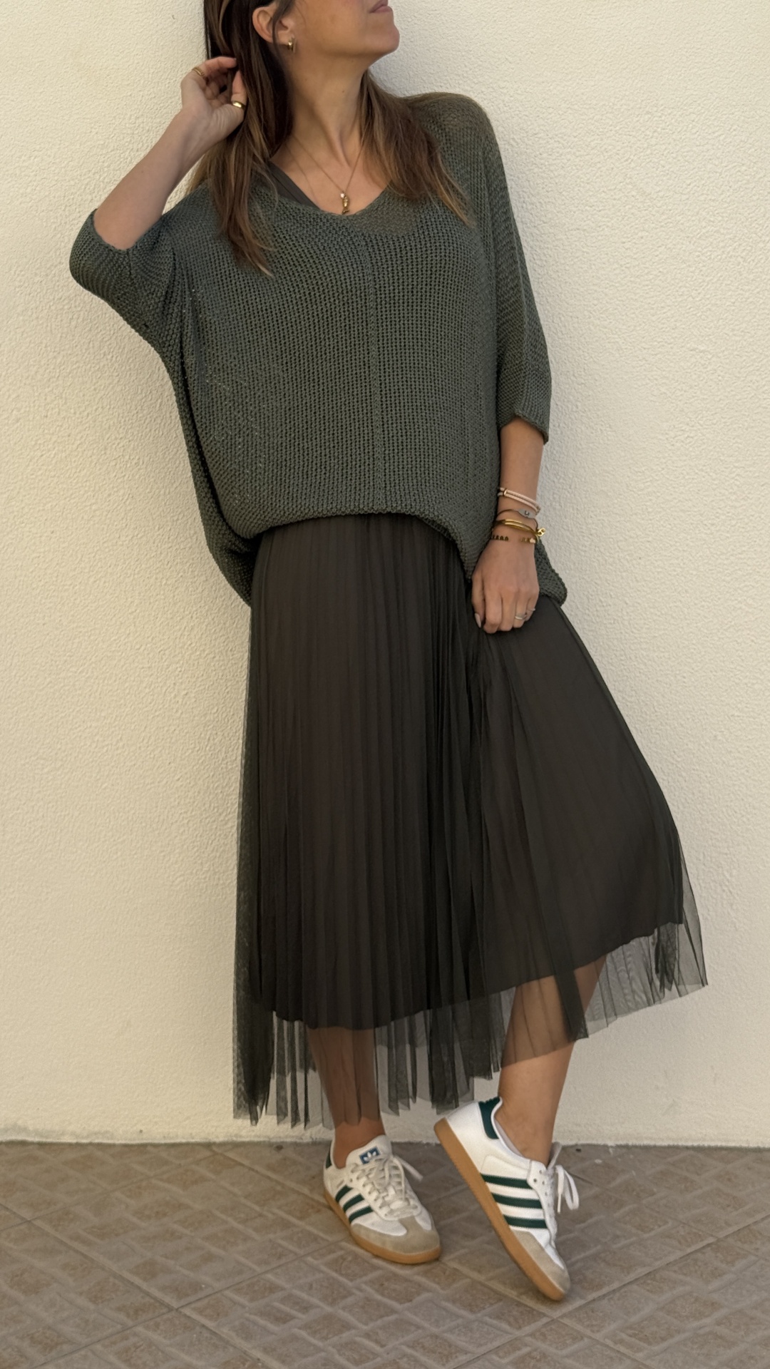 Mulher com camisola verde, saia preta plissada e sapatilhas brancas com riscas verdes
