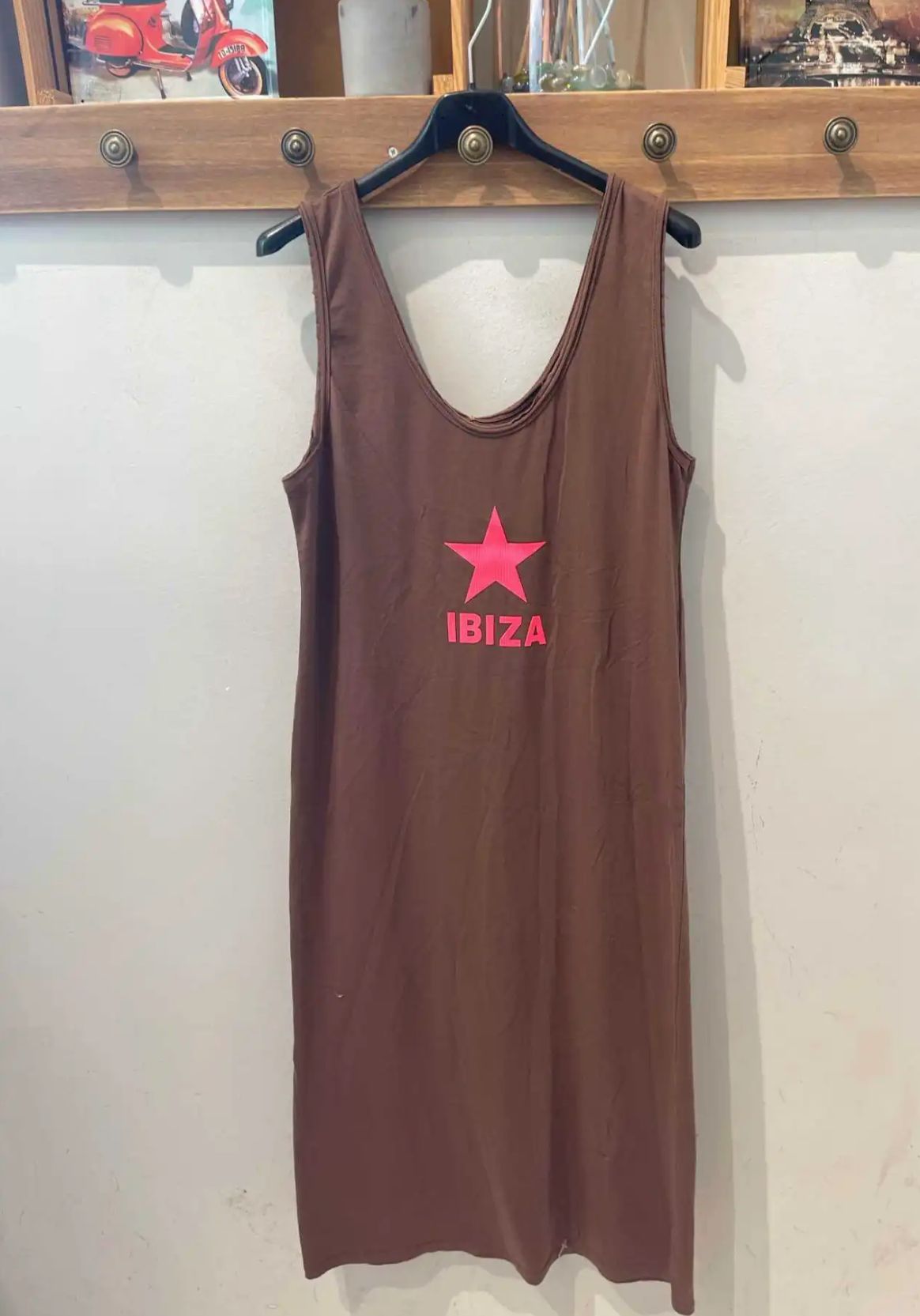 Vestido castanho com estampa rosa estrela e IBIZA pendurado numa parede clara