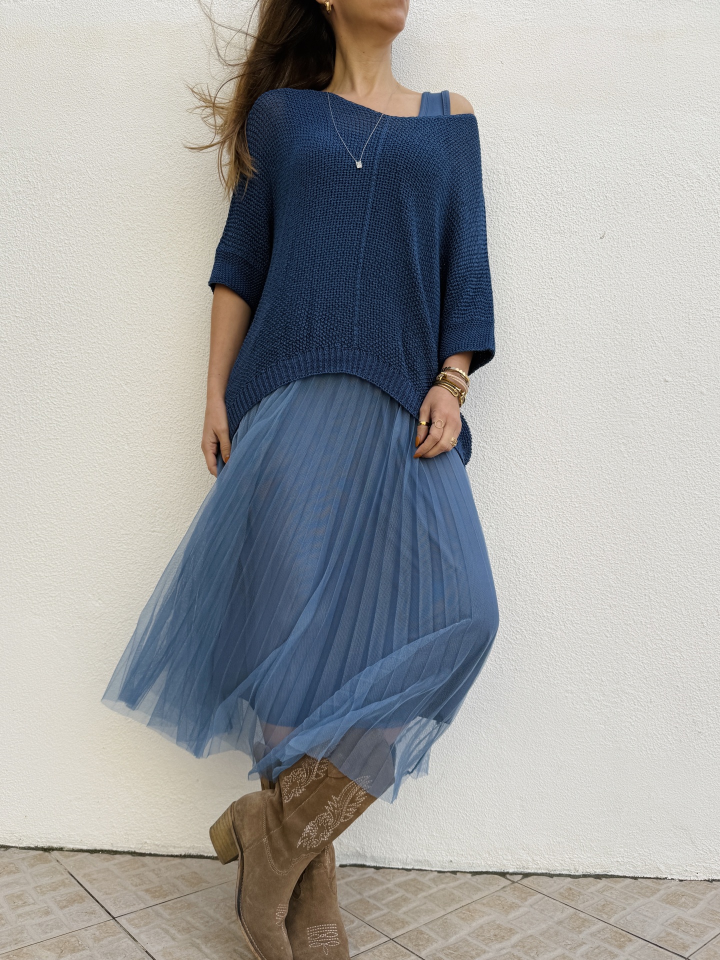 Look com top de malha azul, saia plissada azul e botas castanhas bordadas.