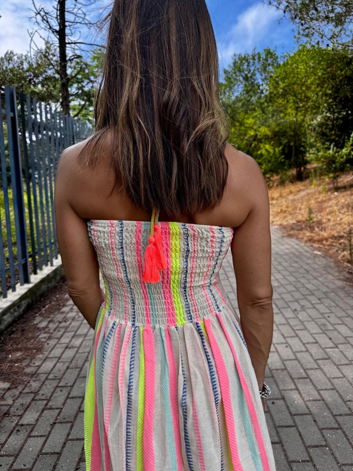 Mulher de costas a usar vestido sem alças colorido com riscas verticais e borla no pescoço.