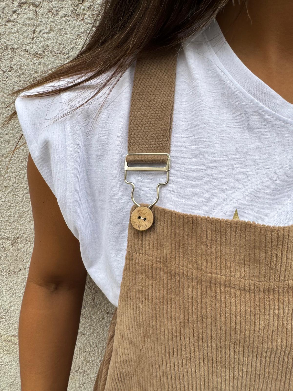 Pessoa com t-shirt branca e macacão castanho claro de veludo cotelê com alças ajustáveis.