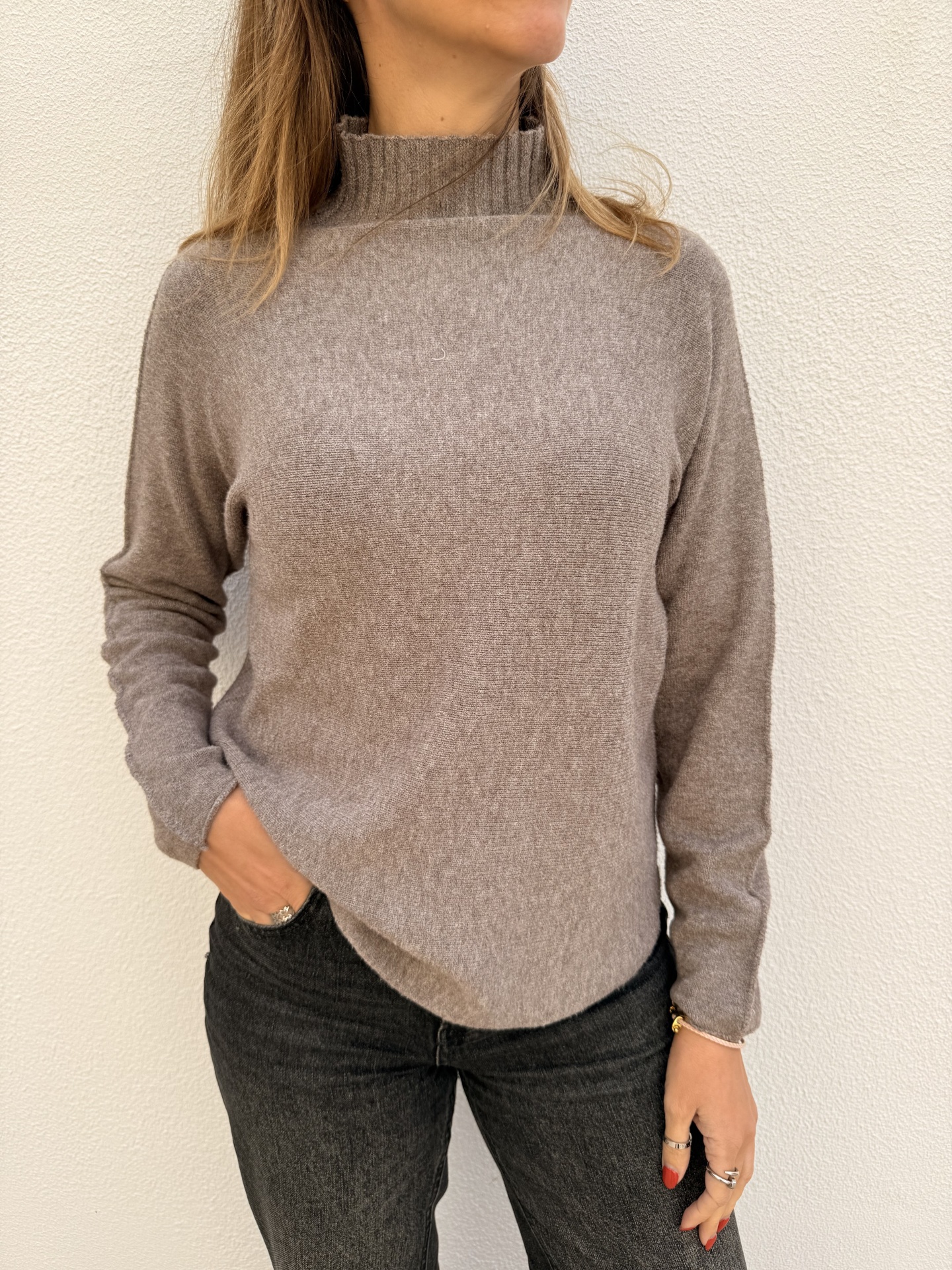 Mulher a usar camisola de malha castanha clara com gola alta e calças pretas em fundo branco