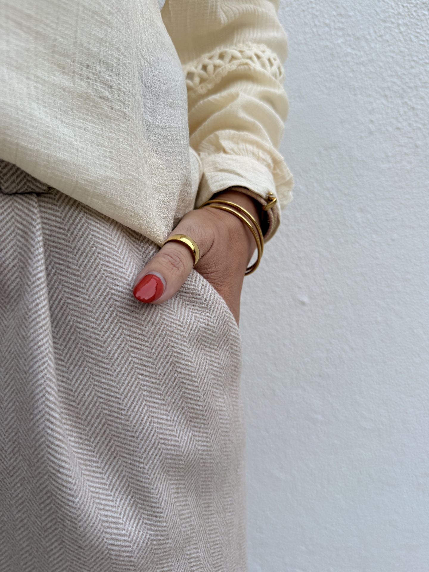 Braço com pulseiras e anel dourado, camisa creme e calças bege padrão espinha de peixe