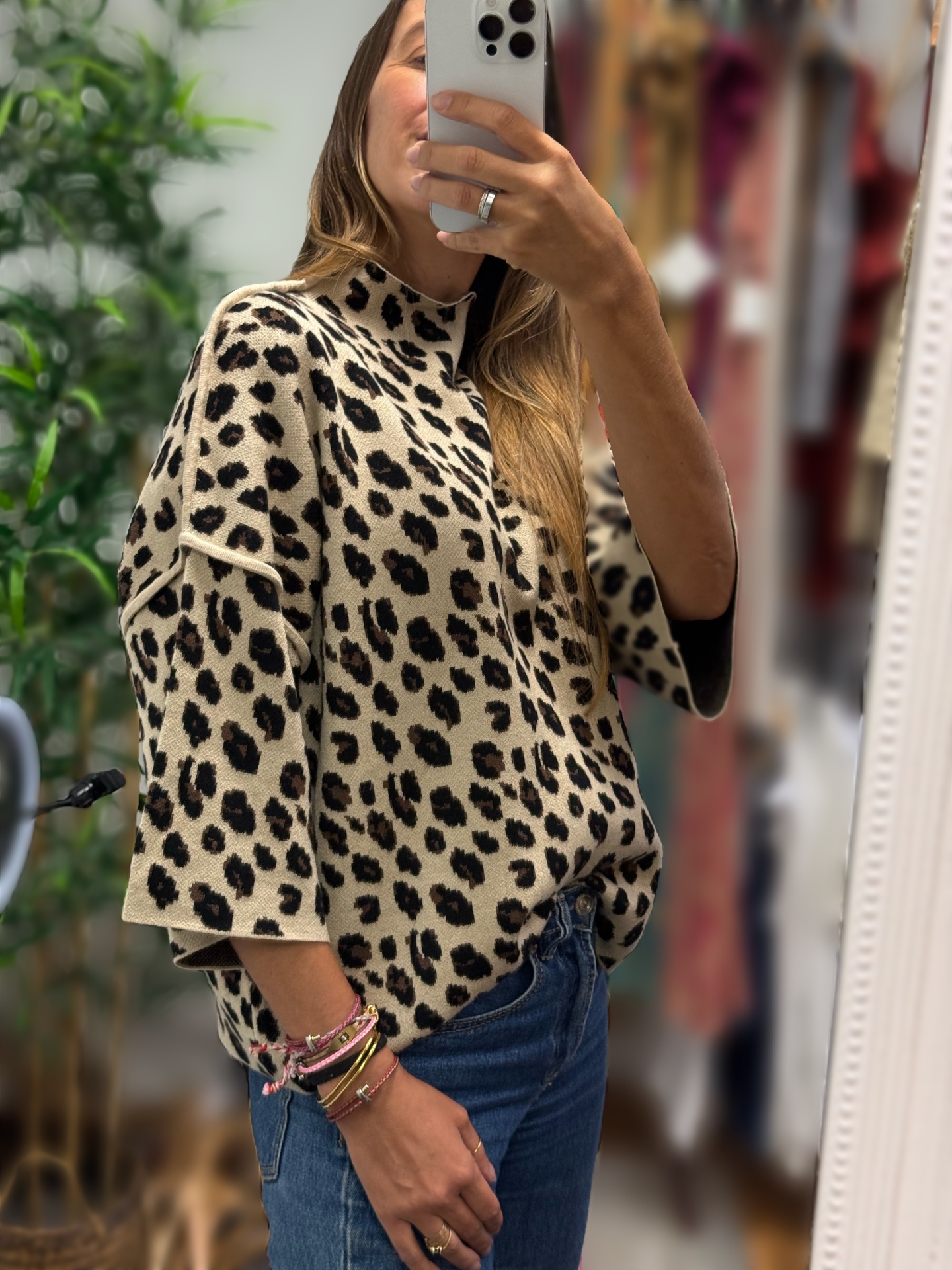 Mulher vestindo camisola animal print bege e preta e jeans azuis à frente de um espelho em ambiente interior