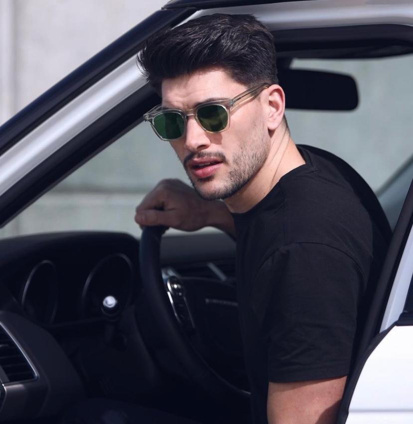 Homem de óculos de sol sentado ao volante de carro branco.