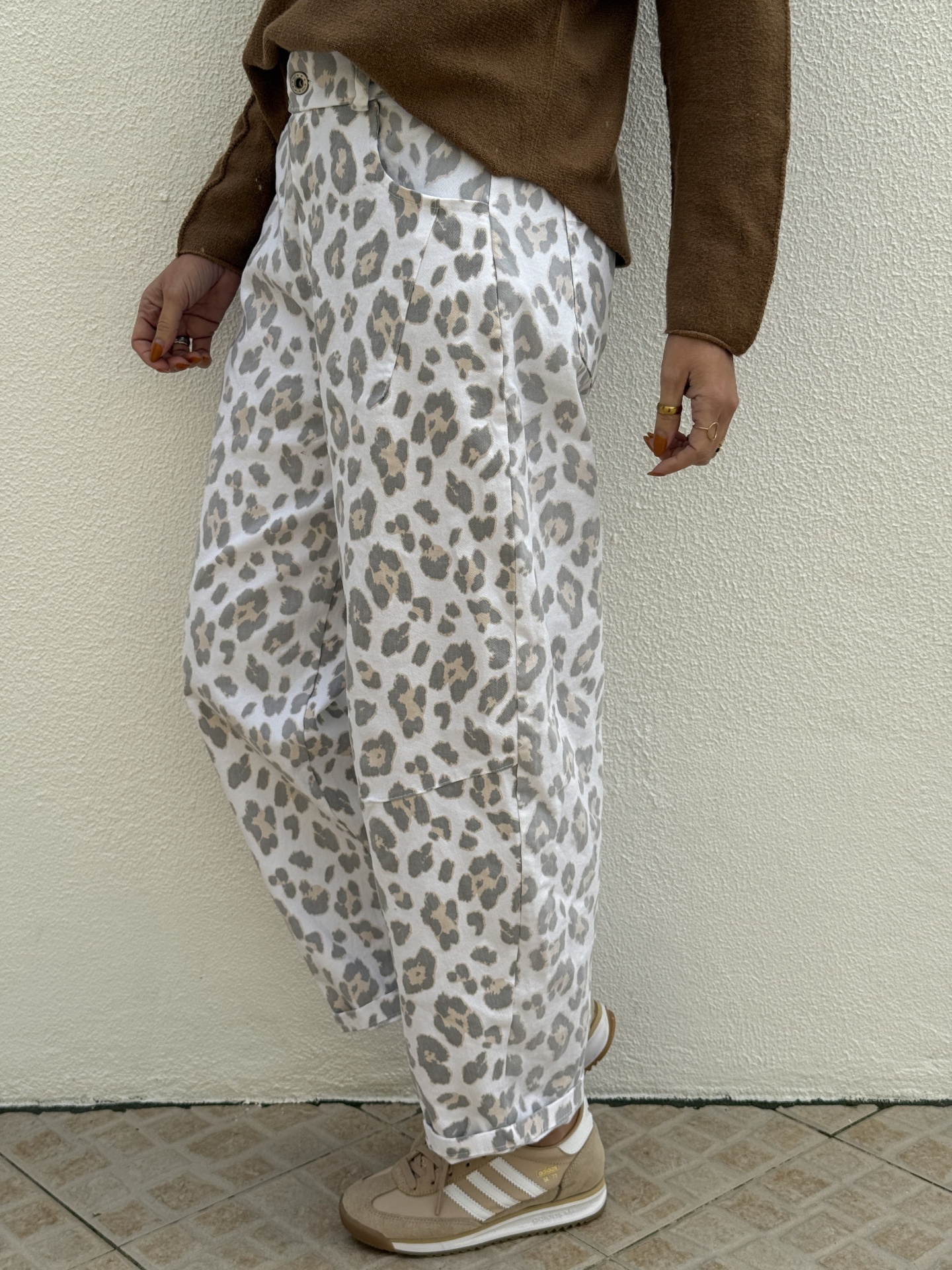 Calças com padrão de leopardo branco e cinza claro com ténis bege adidas e suéter castanho