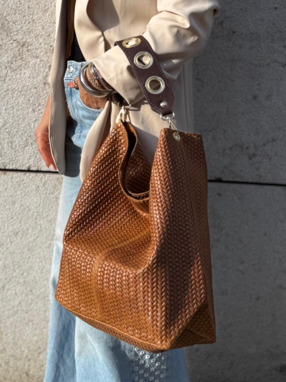Mala castanha trançada com alça de ilhós prateados num cenário urbano