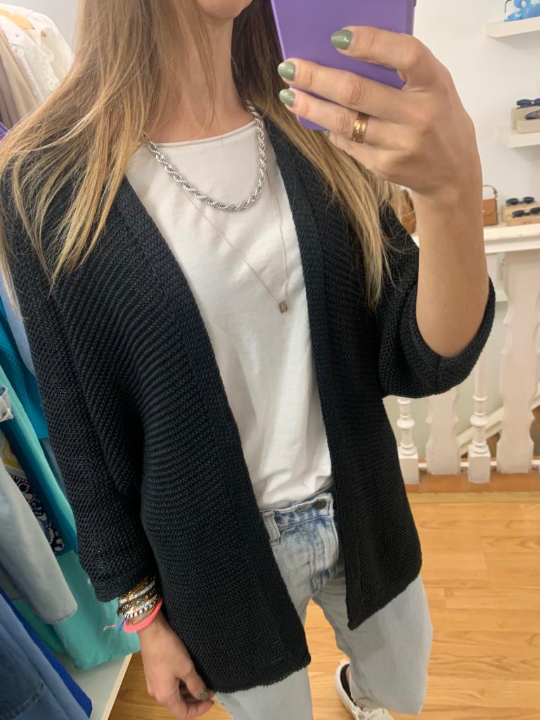 Mulher a usar cardigã preto, t-shirt branca e jeans claros, a tirar selfie com telemóvel roxo num quarto