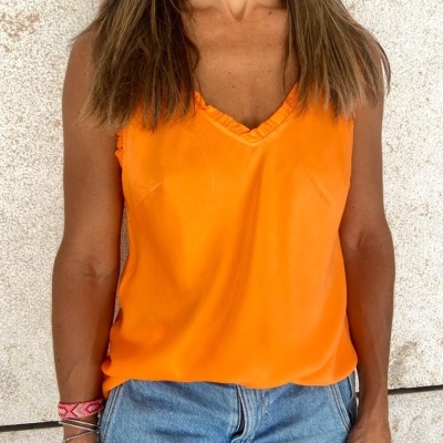 Regata laranja feminina com decote em V e acabamento franzido, calças de ganga azuis, fundo parede clara