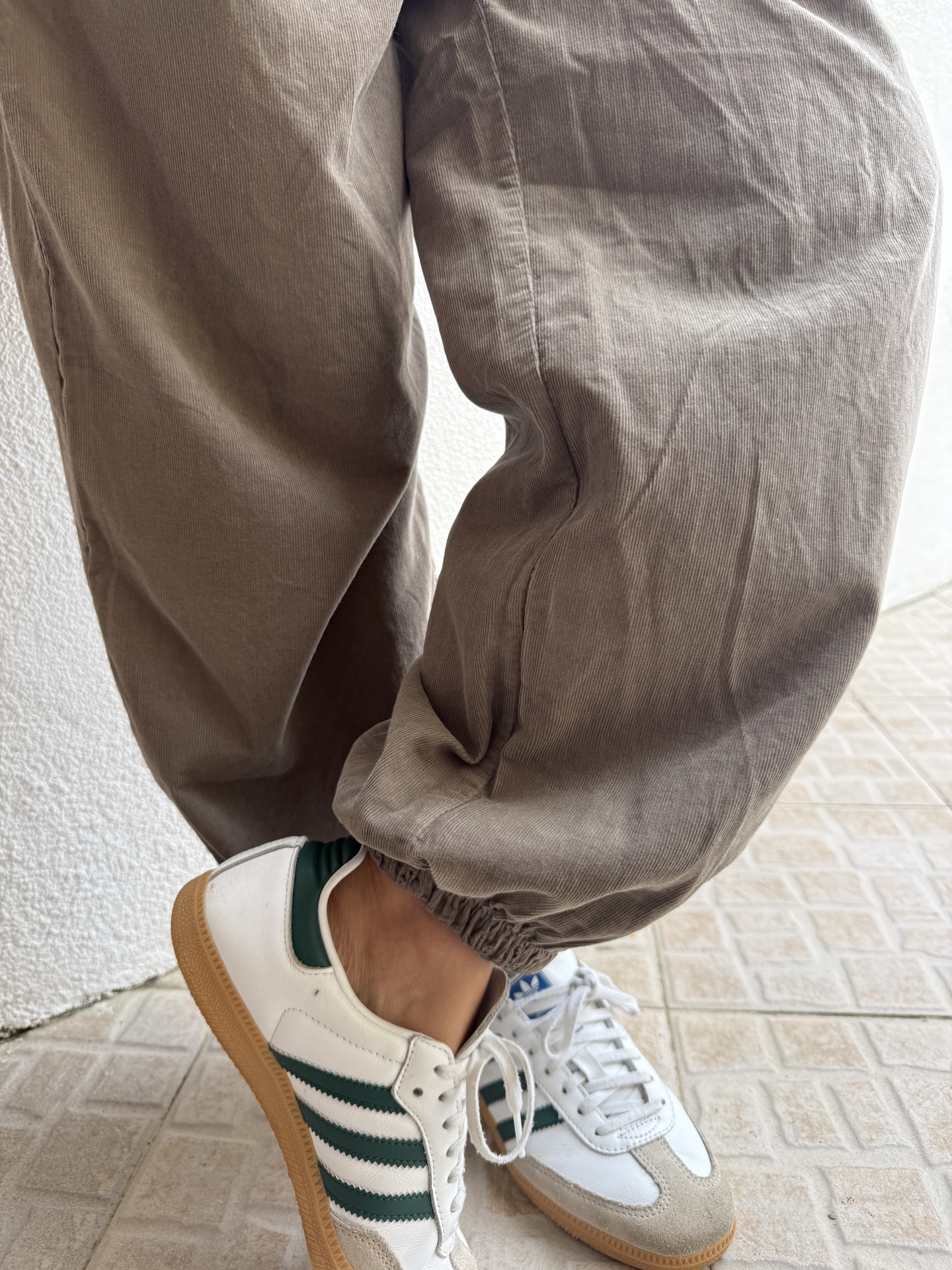 Ténis brancos com riscas verdes e sola castanha usados com calças bege texturizadas