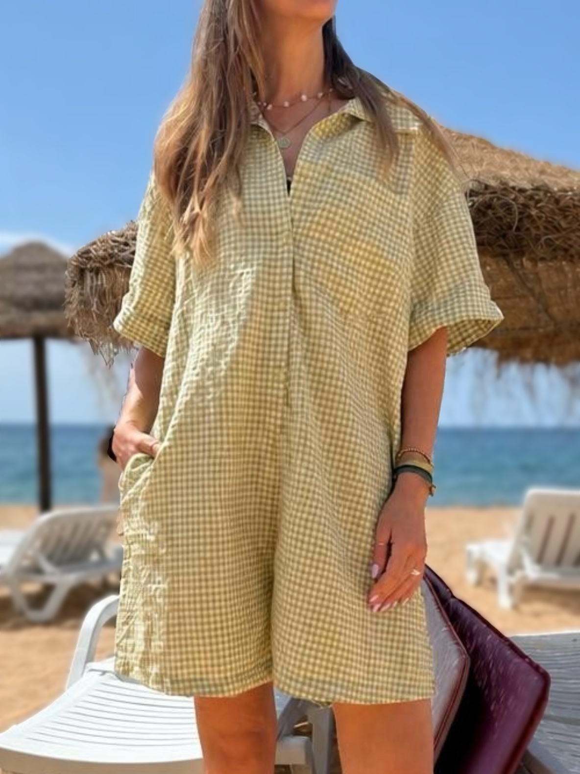 Vestido curto amarelo de padrão xadrez na praia com chapéus de palha e espreguiçadeiras