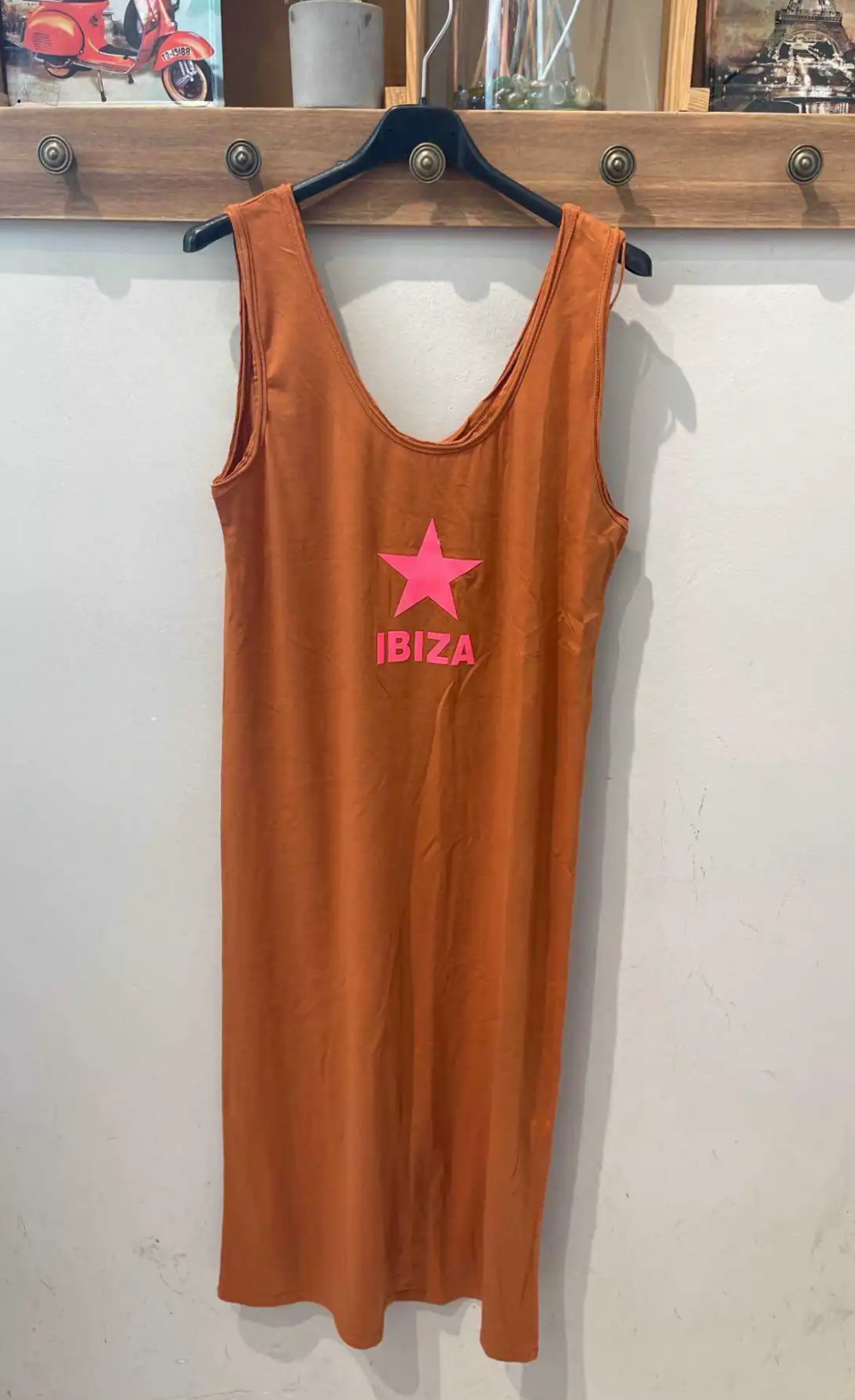 Vestido laranja com estampa rosa IBIZA pendurado num cabide num cabideiro de madeira