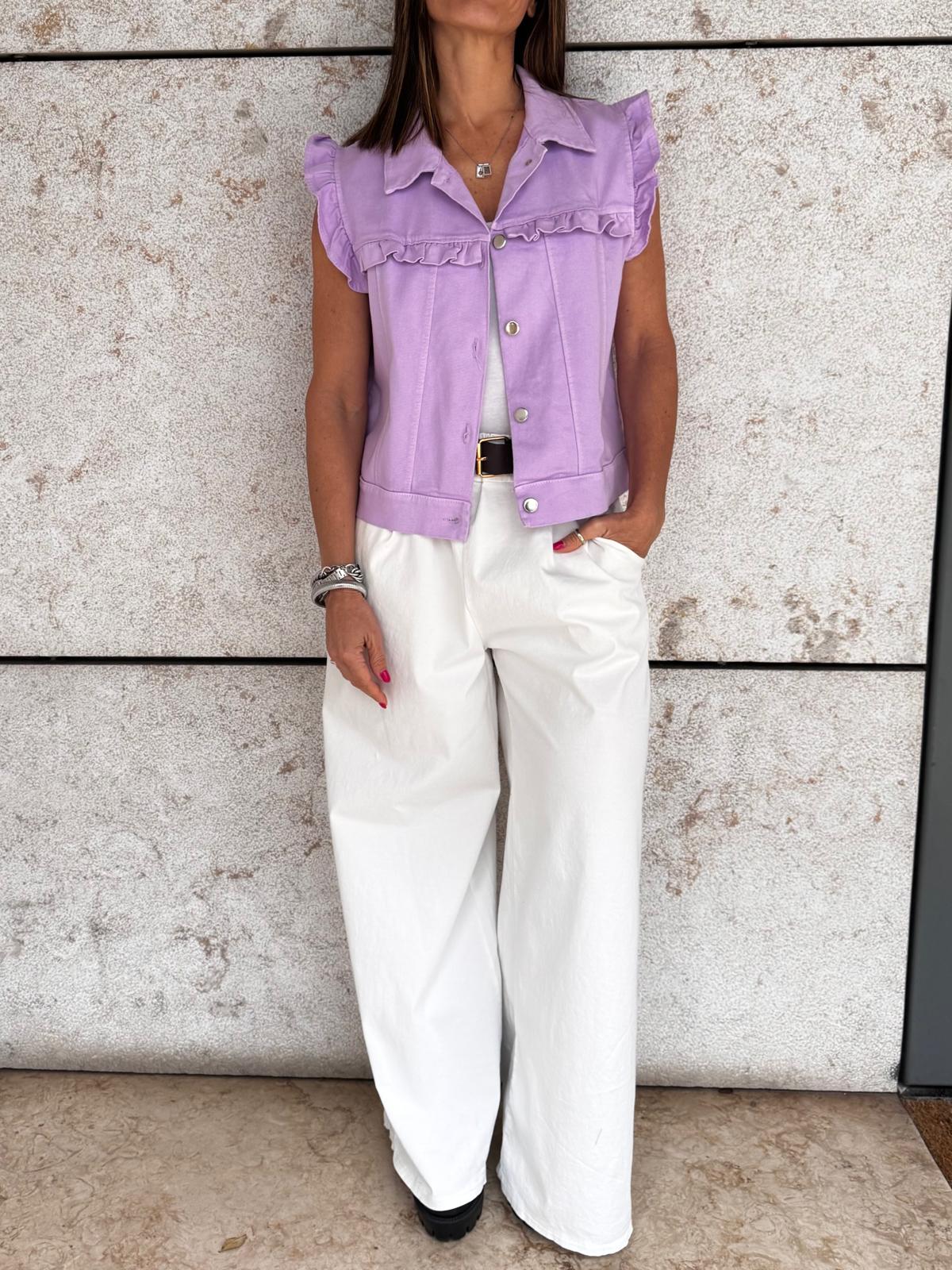 Blusa lilás com folhos e calças brancas largas em fundo de parede de pedra