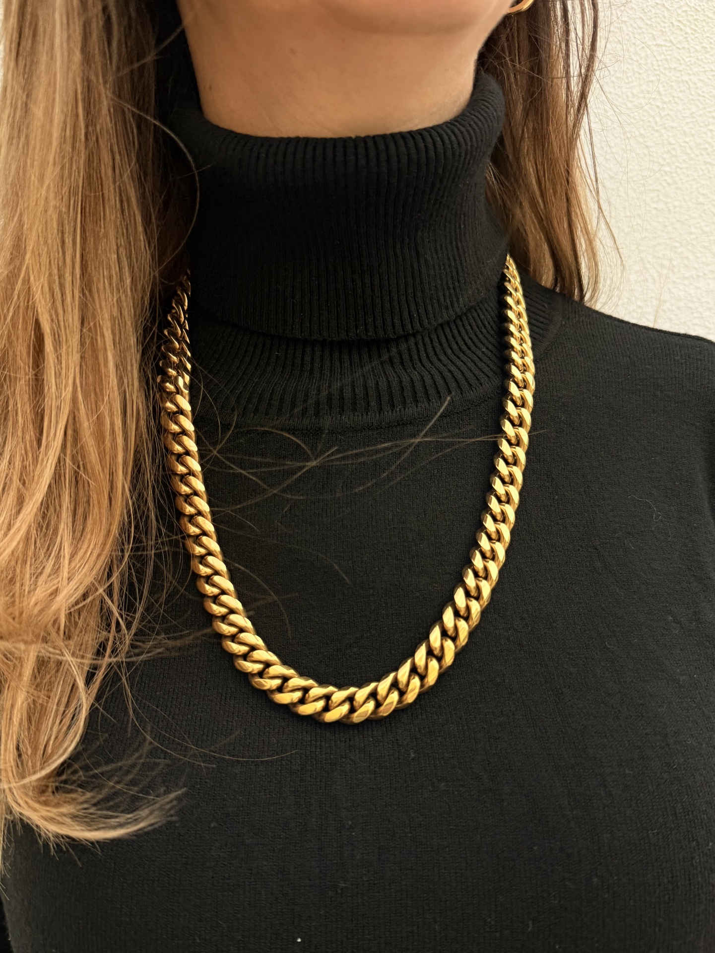 Colar dourado grosso sobre camisola preta de gola alta