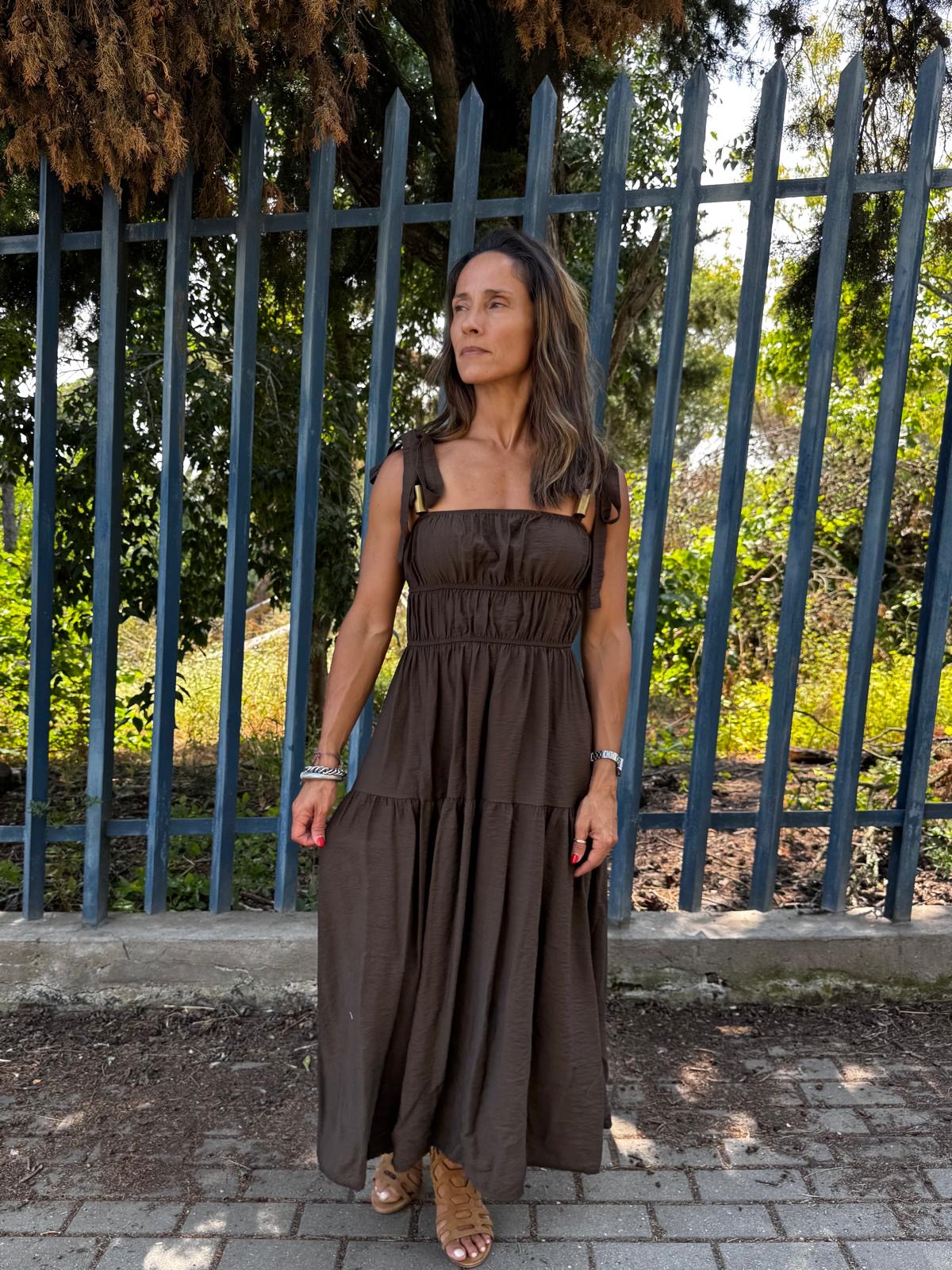 Mulher a usar vestido castanho longo com alças e franzidos em ambiente exterior