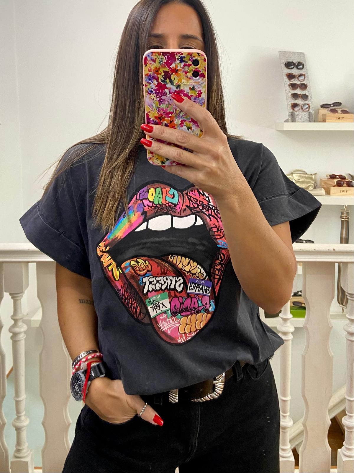 Pessoa com T-shirt preta com estampa de boca colorida, óculos de sol em fundo interior