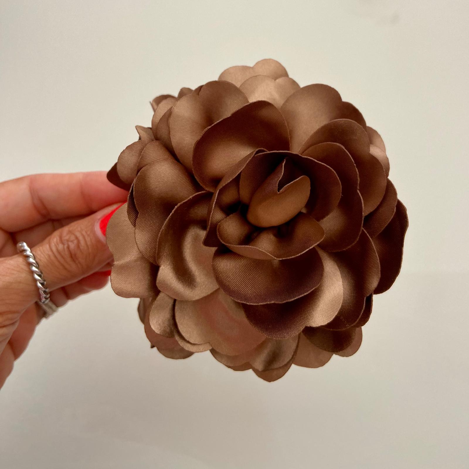 Flor artificial castanha de tecido acetinado segurada por mão contra fundo neutro