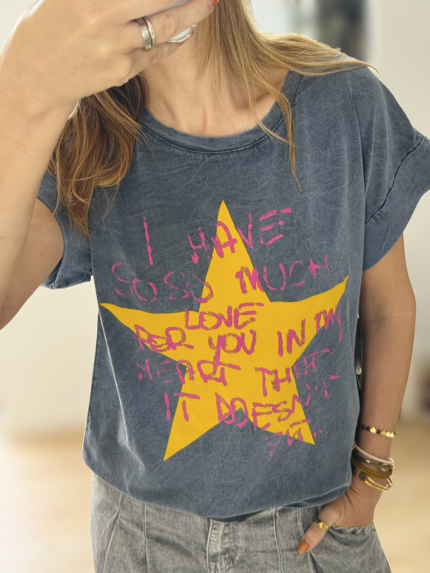 T-shirt azul escura com estrela amarela e texto rosa sendo usada por pessoa com pulseiras e anéis