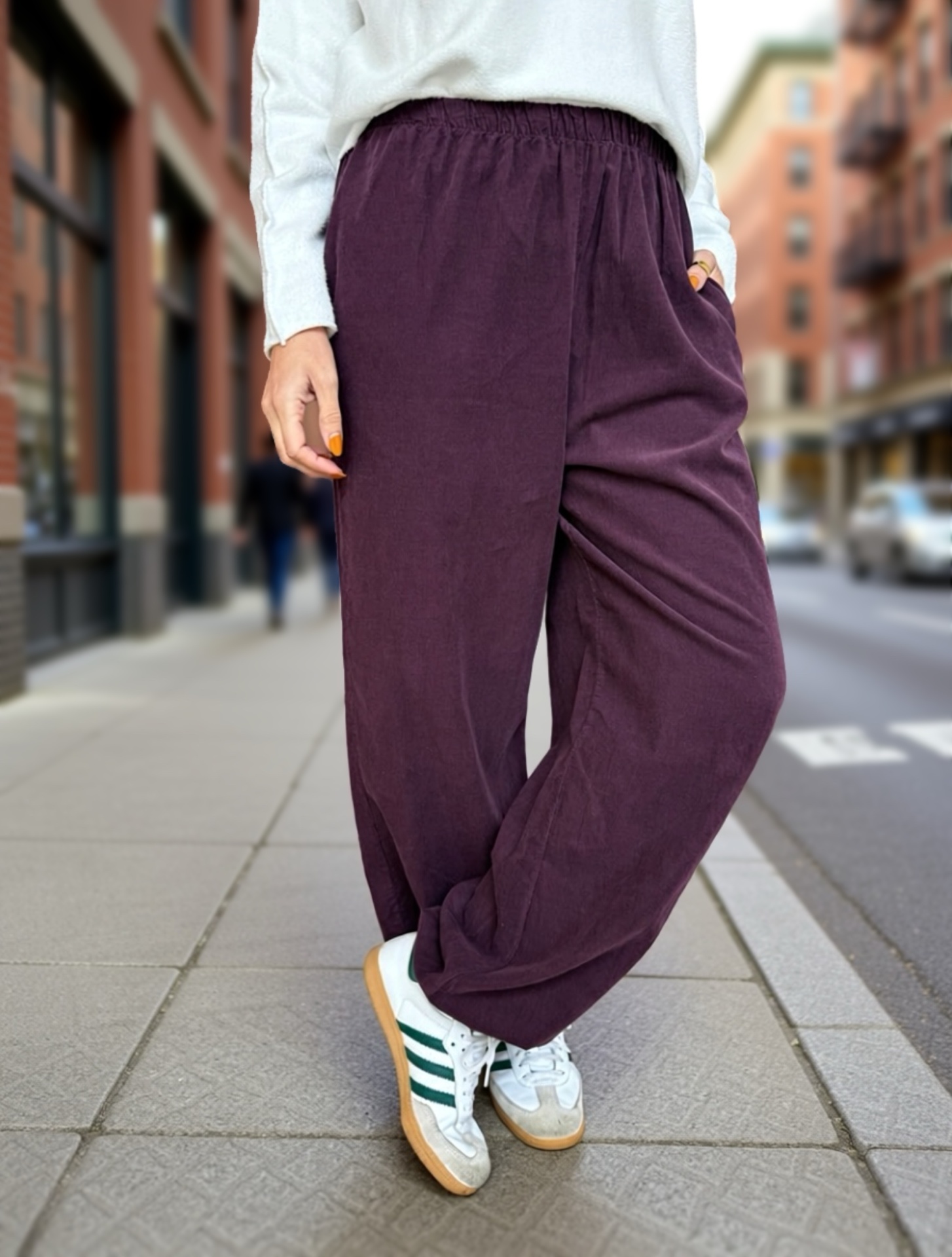 Calças largas roxas em tecido com cós elástico e ténis brancos com riscas verdes na rua