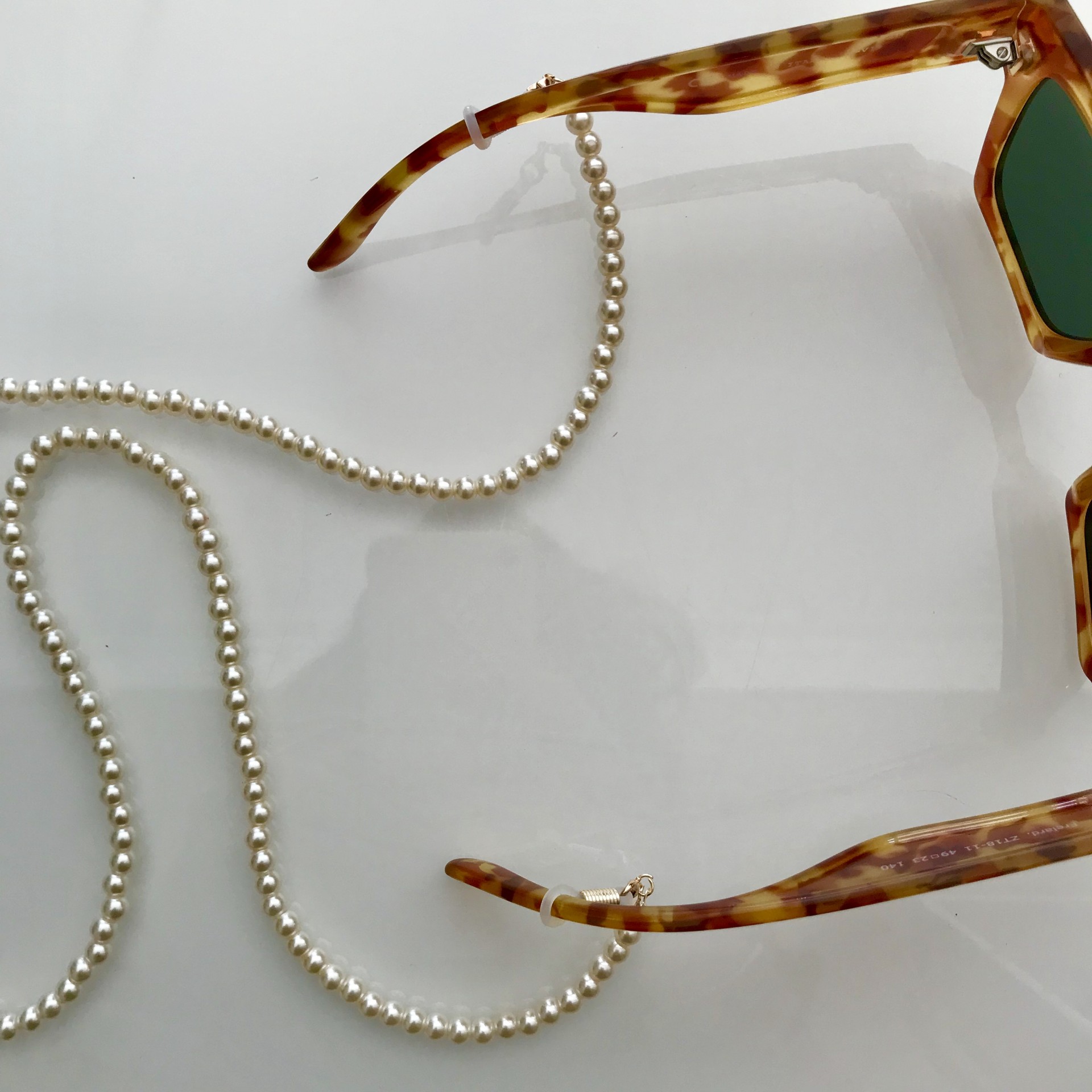 Óculos de sol com corrente de pérolas sobre superfície branca