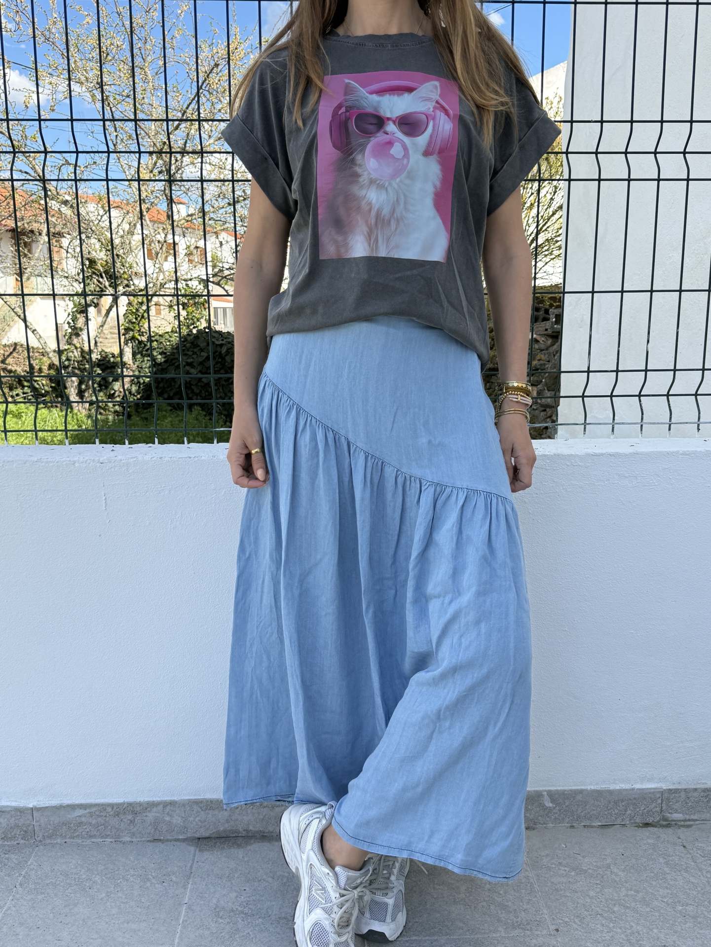 Pessoa com t-shirt cinza escuro estampada de gato rosa e saia longa azul clara