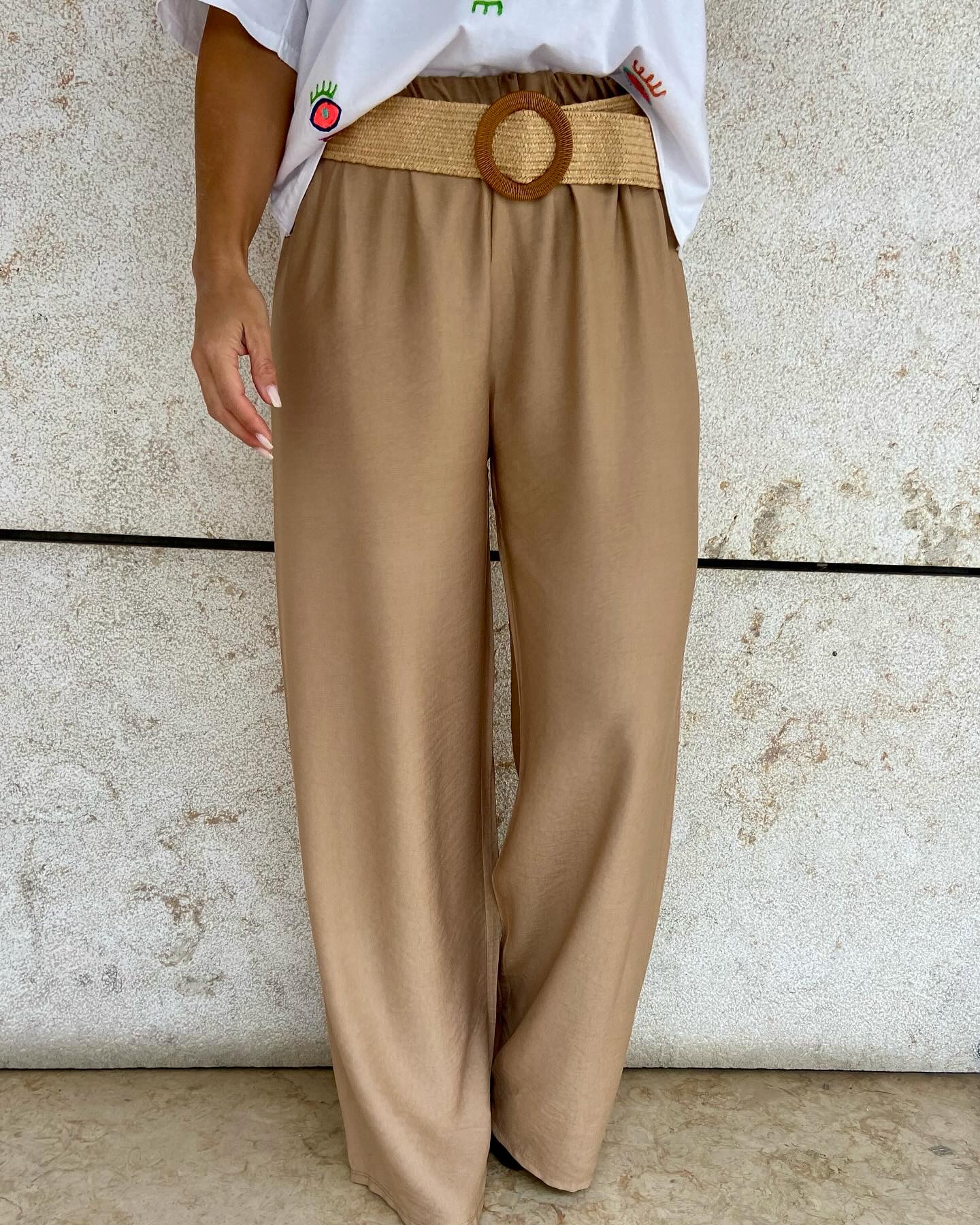 Calças largas camel com cinto bege e fivela redonda em parede de pedra clara
