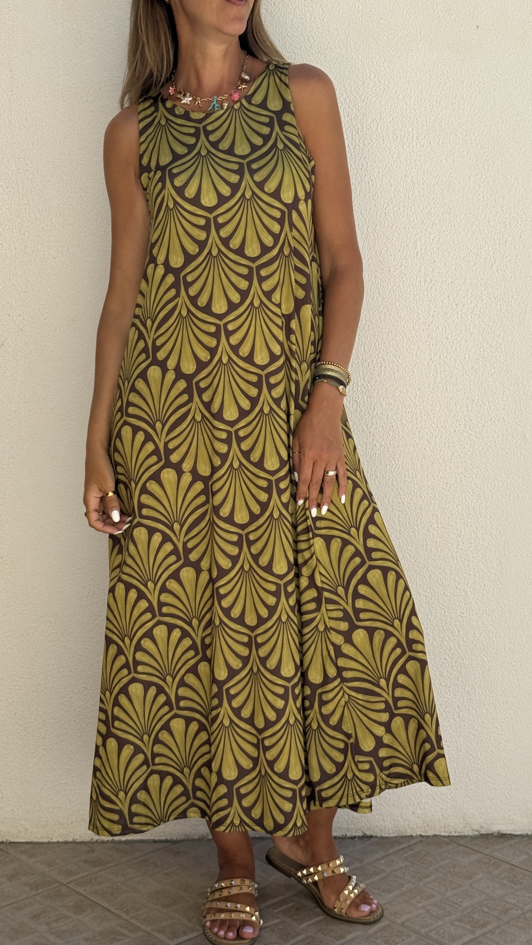 Vestido longo com padrão dourado e castanho, mulher com pulseiras e colar, sandálias douradas