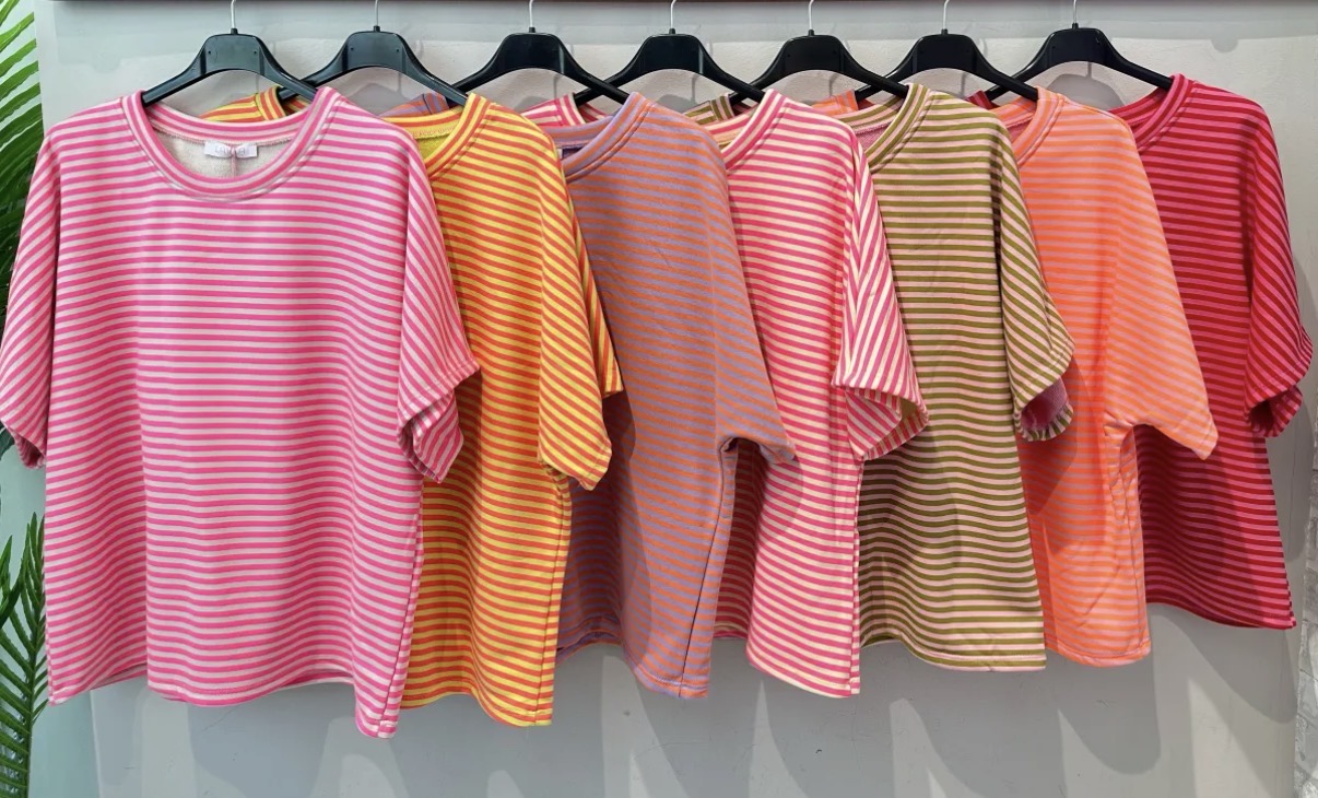 Sete t-shirts de riscas coloridas penduradas em cabides pretos