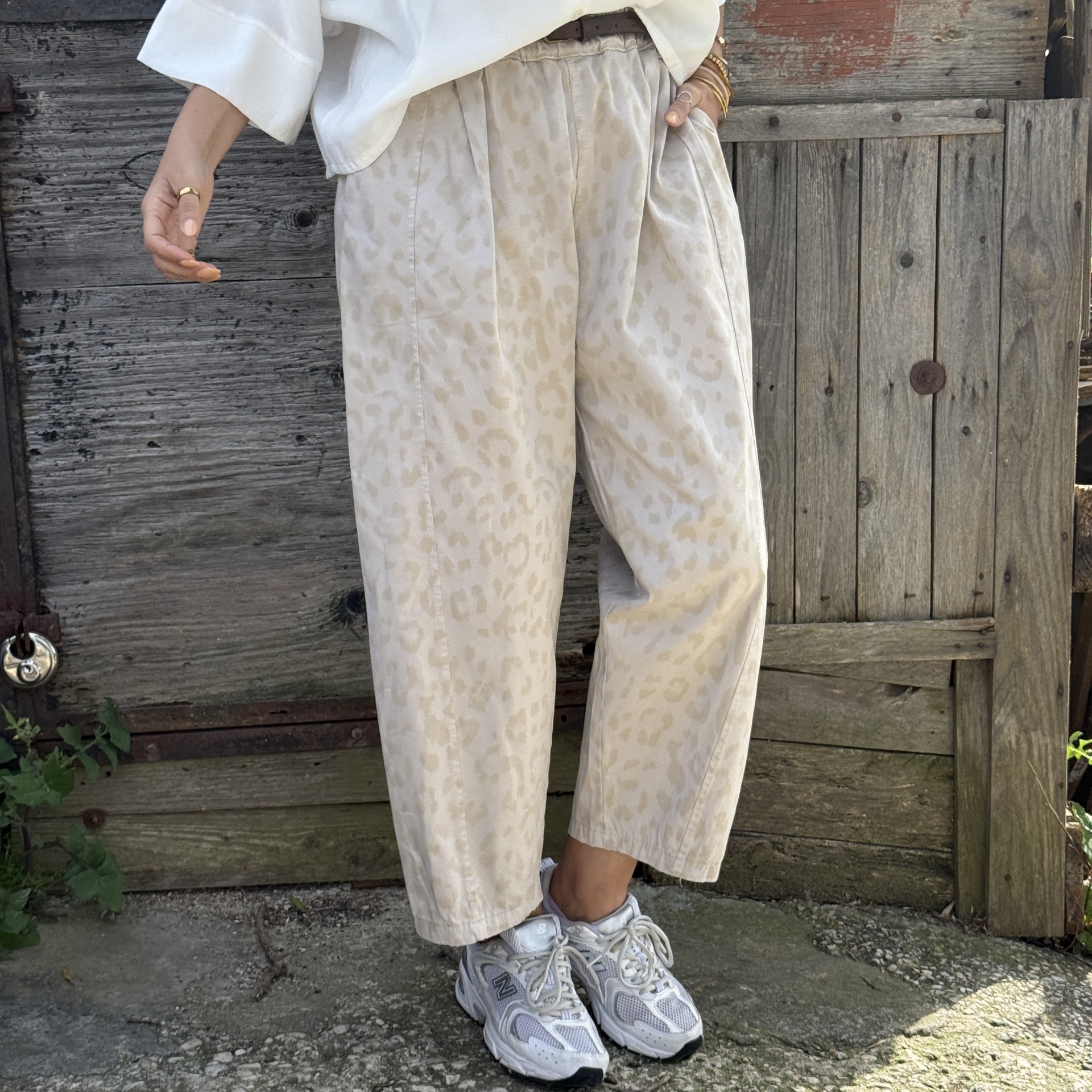 Calças compridas bege com padrão leopardo subtil e ténis desportivos cinza em fundo de madeira envelhecida