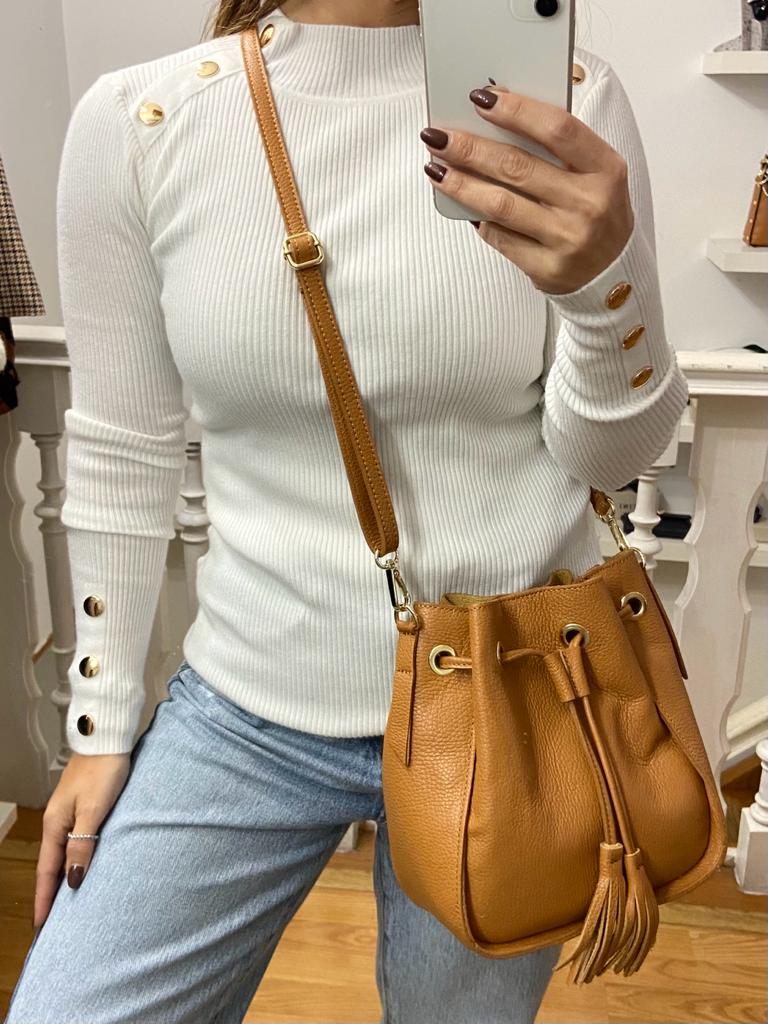 Mulher com camisola branca, calças de ganga azuis e mala castanha em pele em ambiente interior