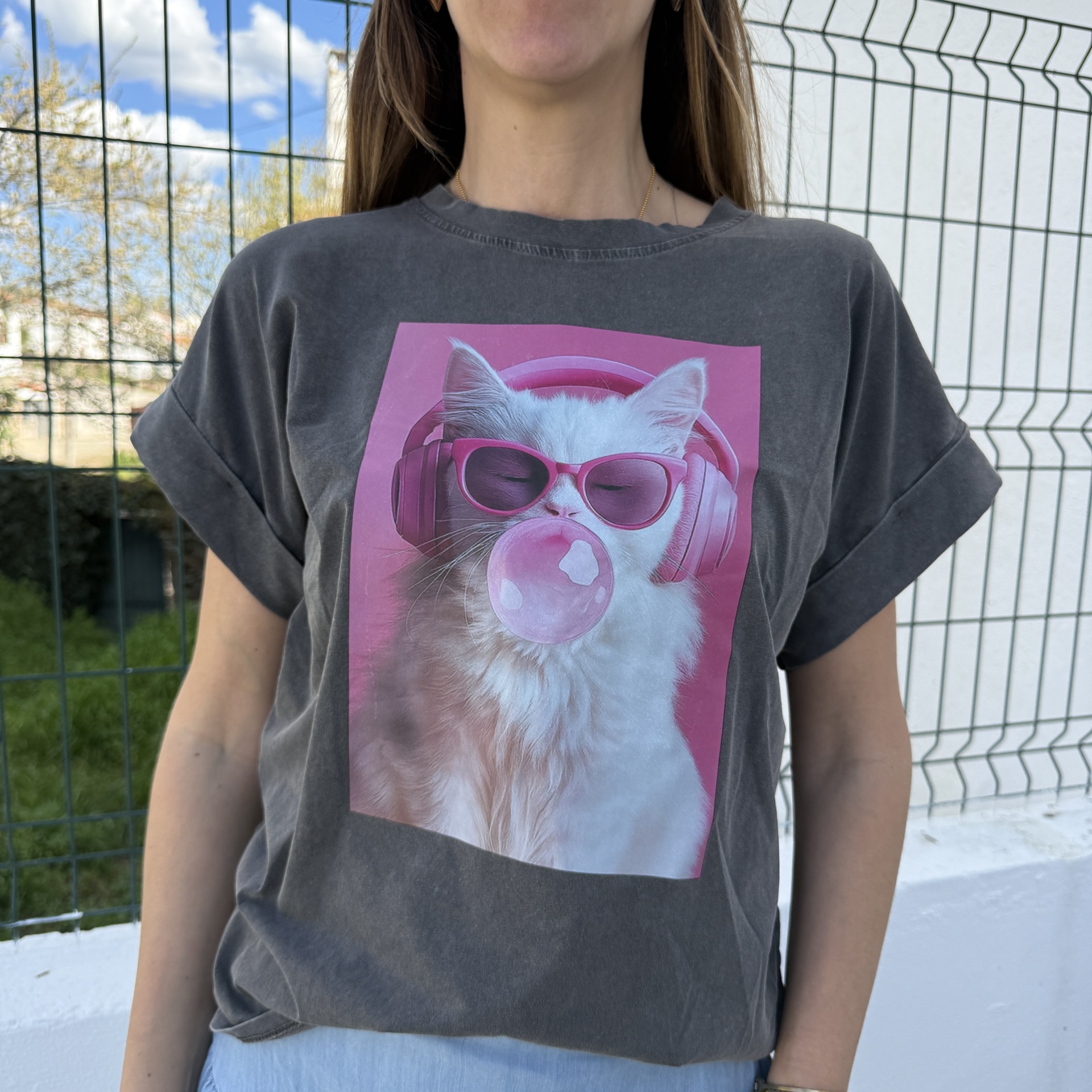 T-shirt cinza com estampa de gato branco com auscultadores e óculos de sol rosa a mascar pastilha elástica.