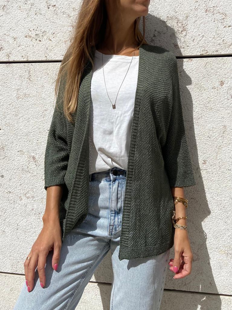 mulher com casaco de malha verde e jeans contra parede clara