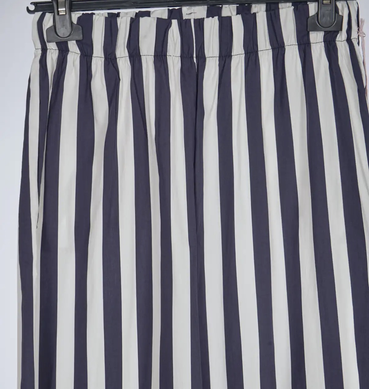 Saia às riscas verticais azul escuro e branco com cintura elástica pendurada num cabide.