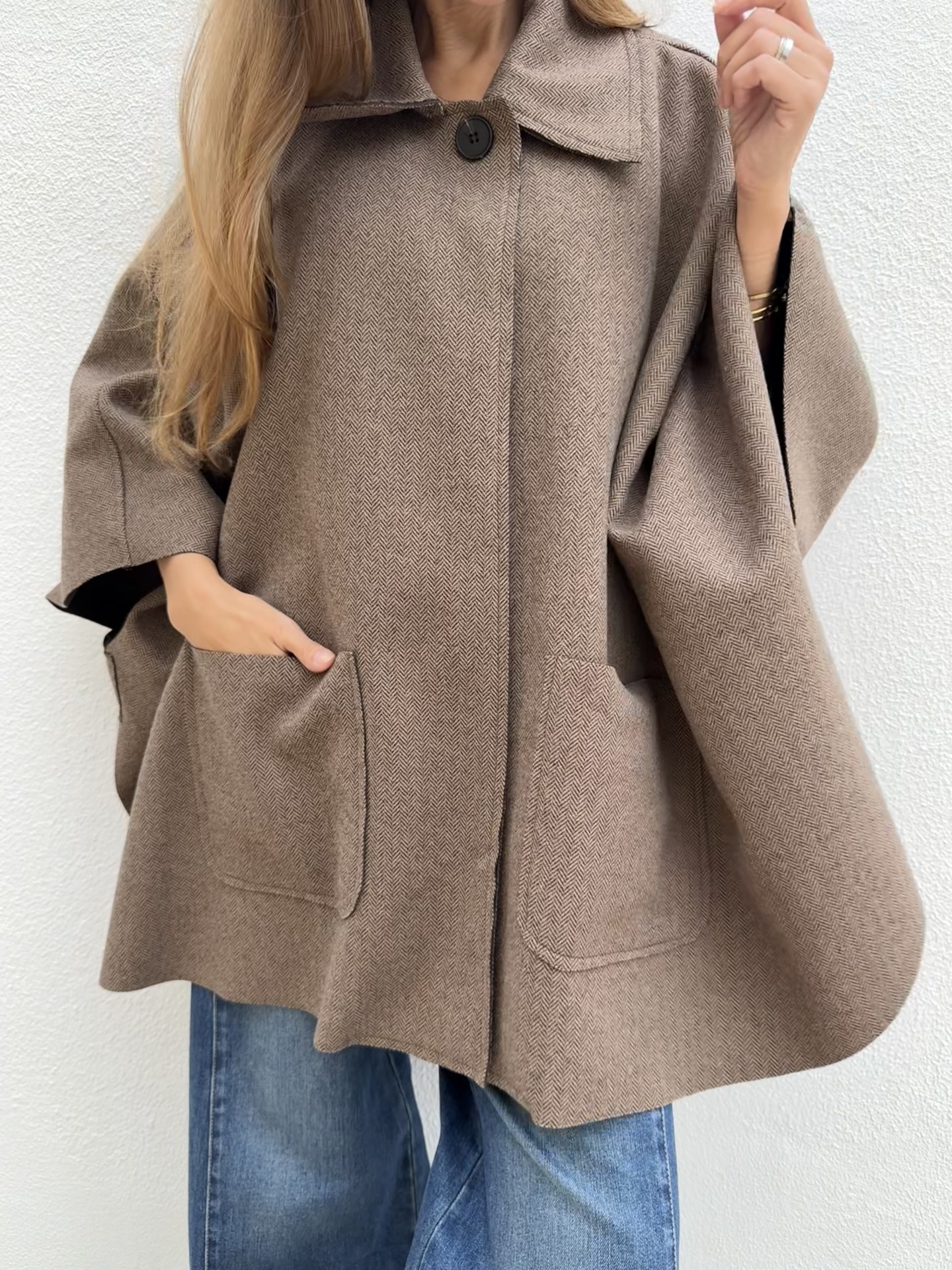 Capa ou poncho castanho com padrão espinha de peixe e bolso frontal, usado com jeans azuis