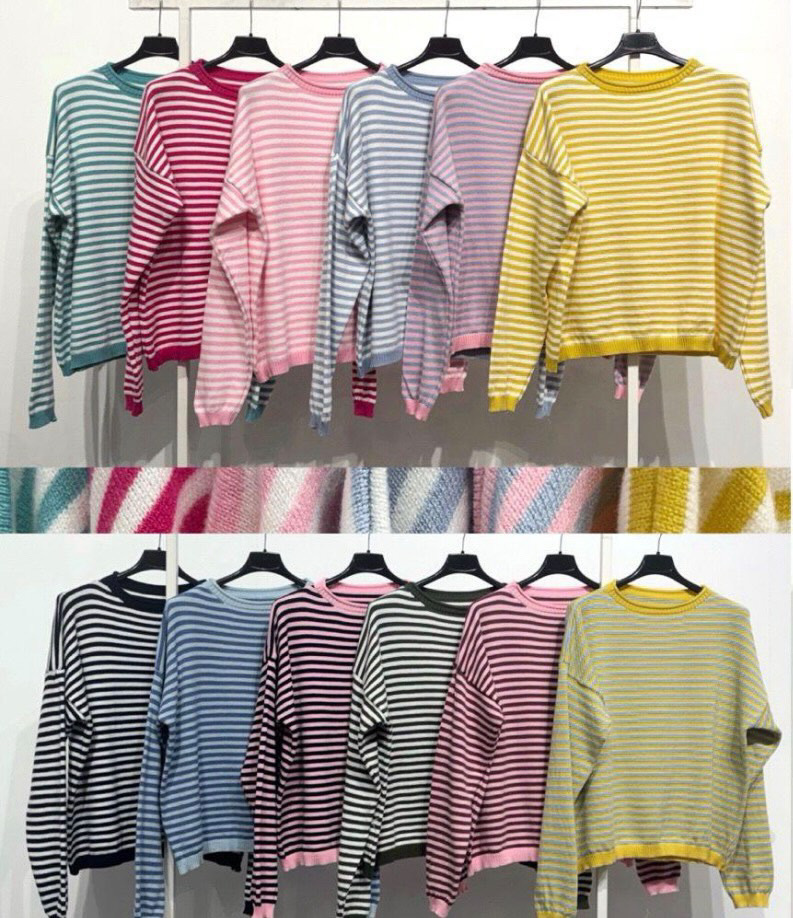 Camisolas de manga comprida às riscas em várias cores penduradas em cabides num fundo branco.