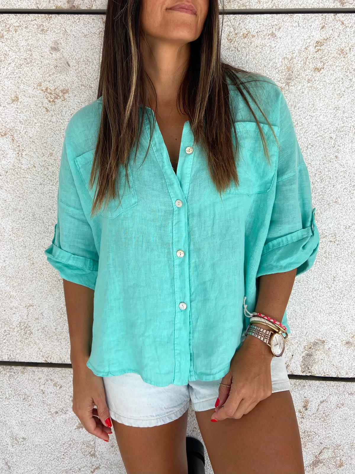 Mulher de camisa azul turquesa e calções brancos contra parede clara