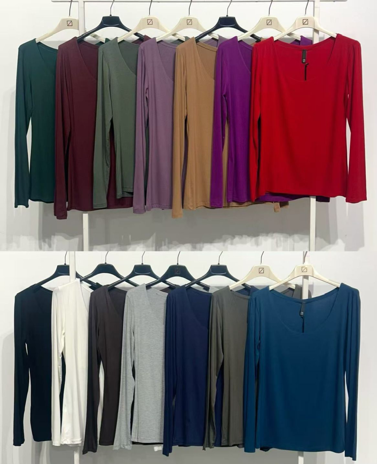Camisolas de manga comprida em várias cores penduradas em cabides numa parede branca.