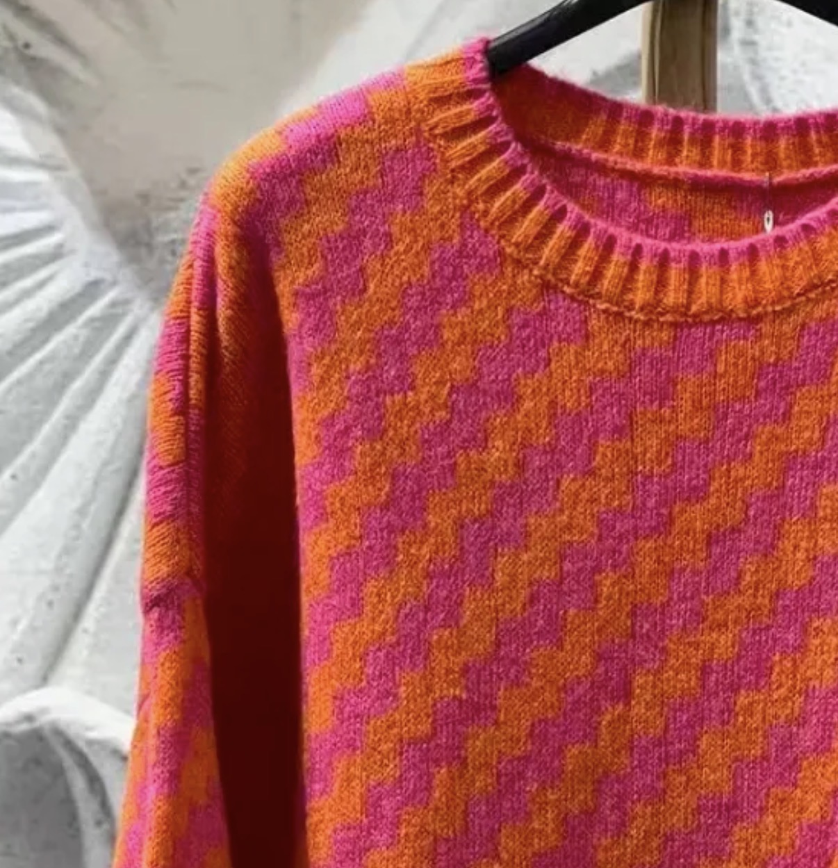 Camisola de malha laranja e rosa com padrão geométrico pendurada num cabide