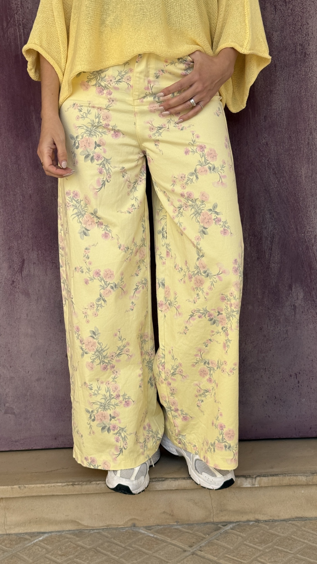 Calças amarelas com padrão floral rosa e verde e ténis brancos