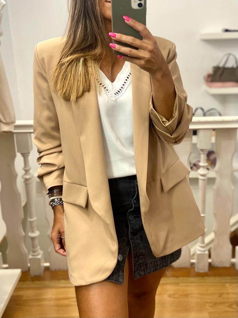 Mulher com casaco bege, blusa branca e saia preta a tirar selfie num espelho