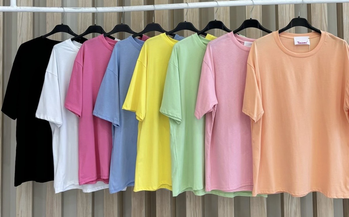 Sete t-shirts coloridas de manga curta em cabides suspensos.