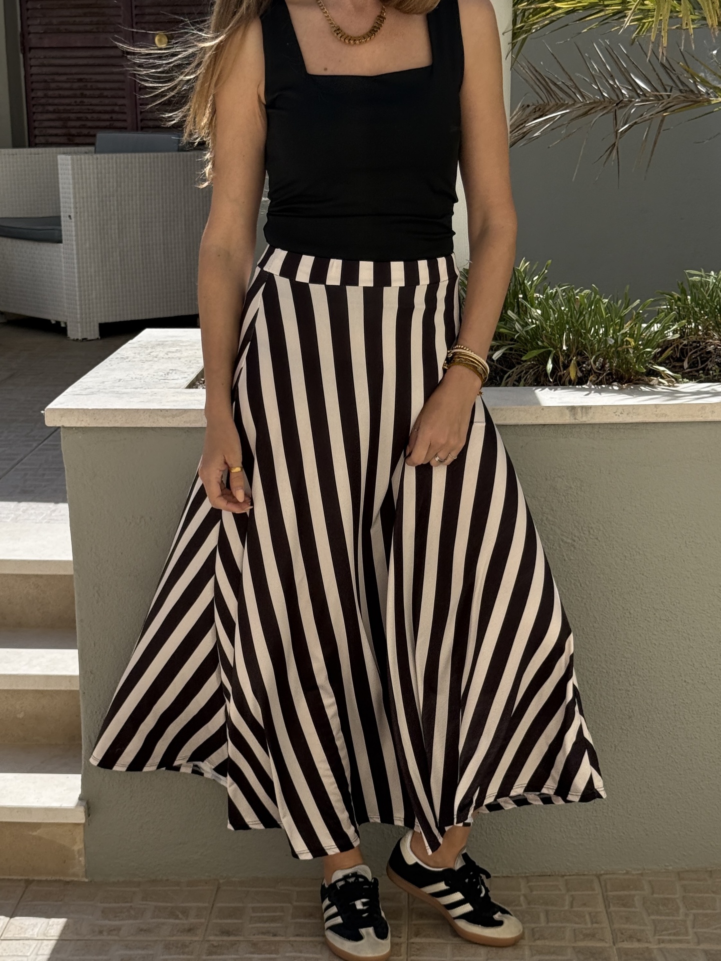 Mulher com saia preta e branca riscada, top preto e ténis brancos e pretos em ambiente exterior